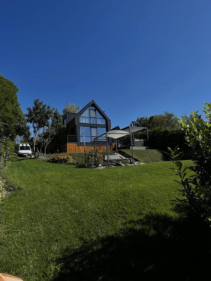 A finished garden with a view, a mown lawn, hedging and shading, in front of a modern pitched-roof house
